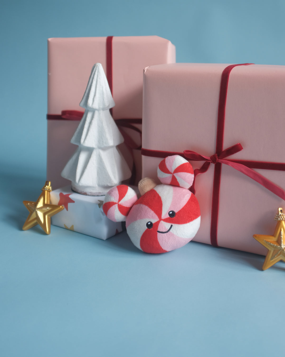 Peppermint Pal bag charm among pink gift boxes, a white tree and gold star ornaments