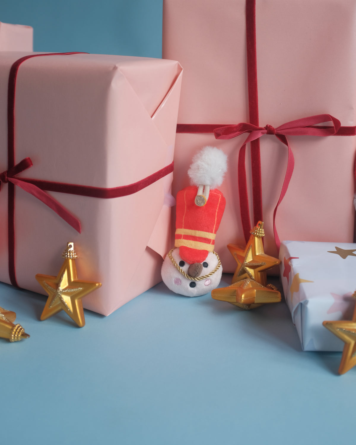 The Merry Marcher bag charm beside pink gift boxes and gold star ornaments
