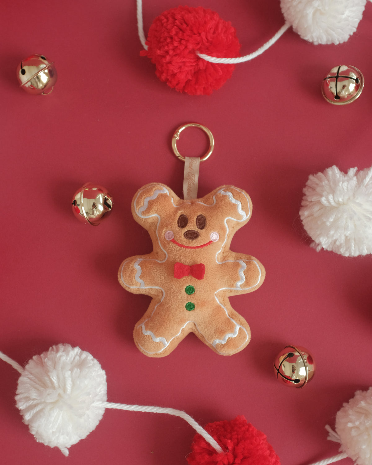Gingerbread Gent bag charm with a white pom-pom garland and gold jingle bells on red