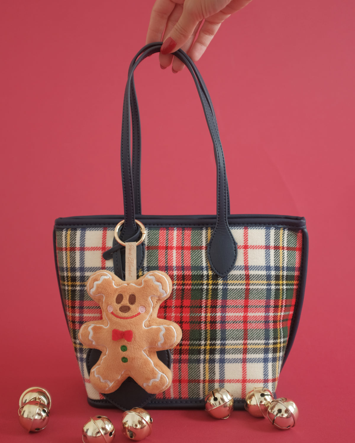 Gingerbread Gent bag charm clipped to a plaid tote, with gold jingle bells