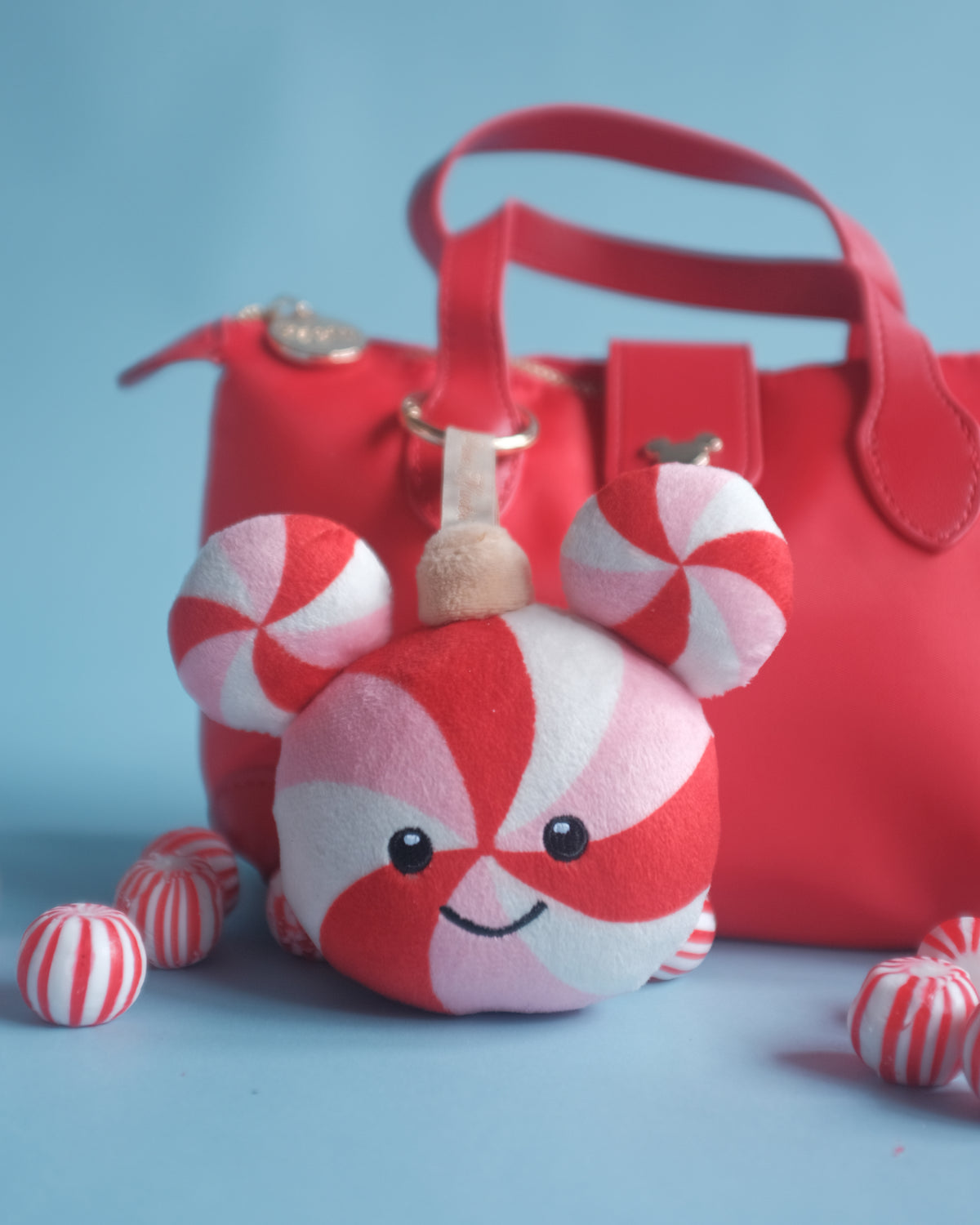 Close-up of the Peppermint Pal bag charm on a red handbag, peppermint candies scattered around