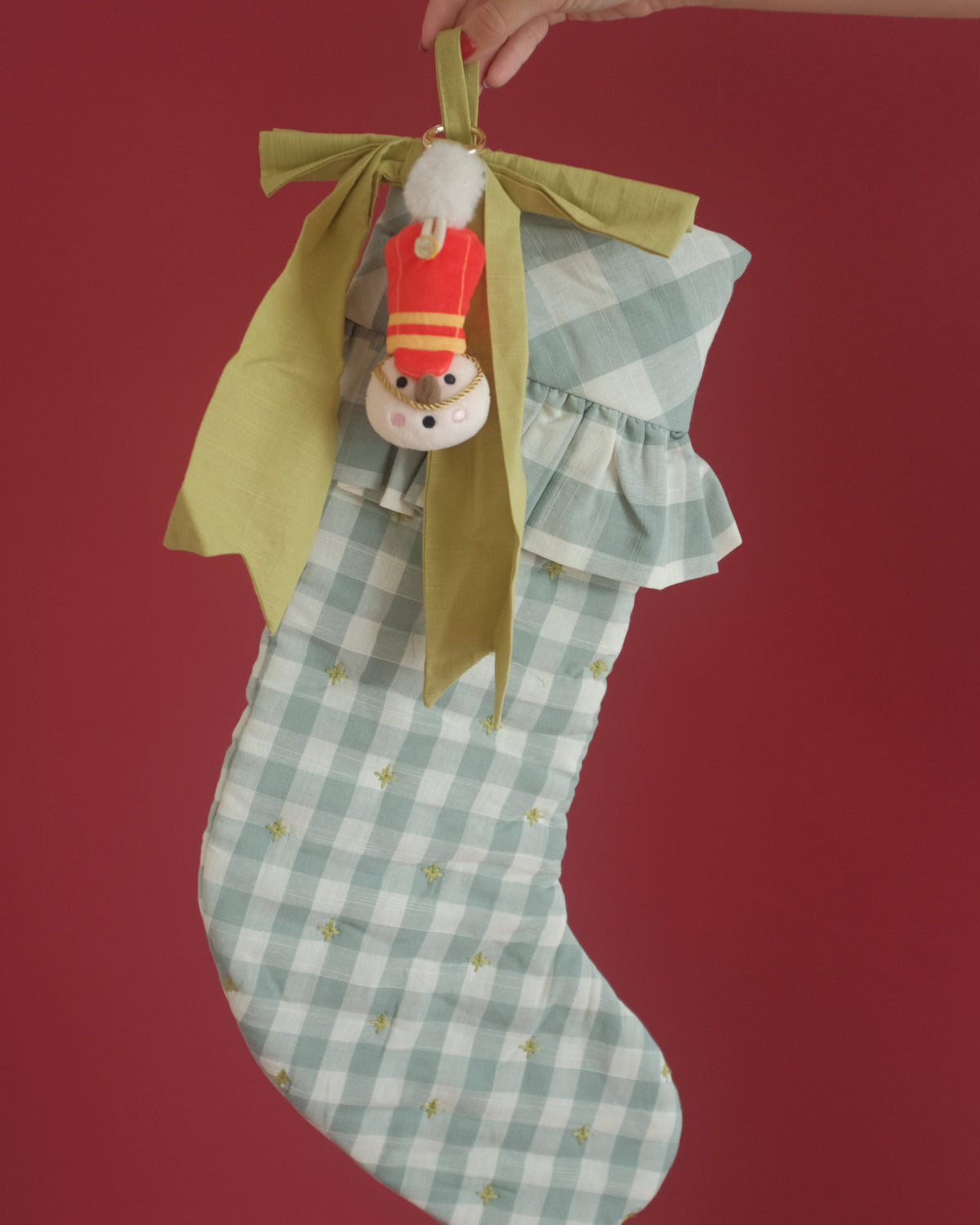 The Merry Marcher bag charm hanging from a green bow on a gingham Christmas stocking
