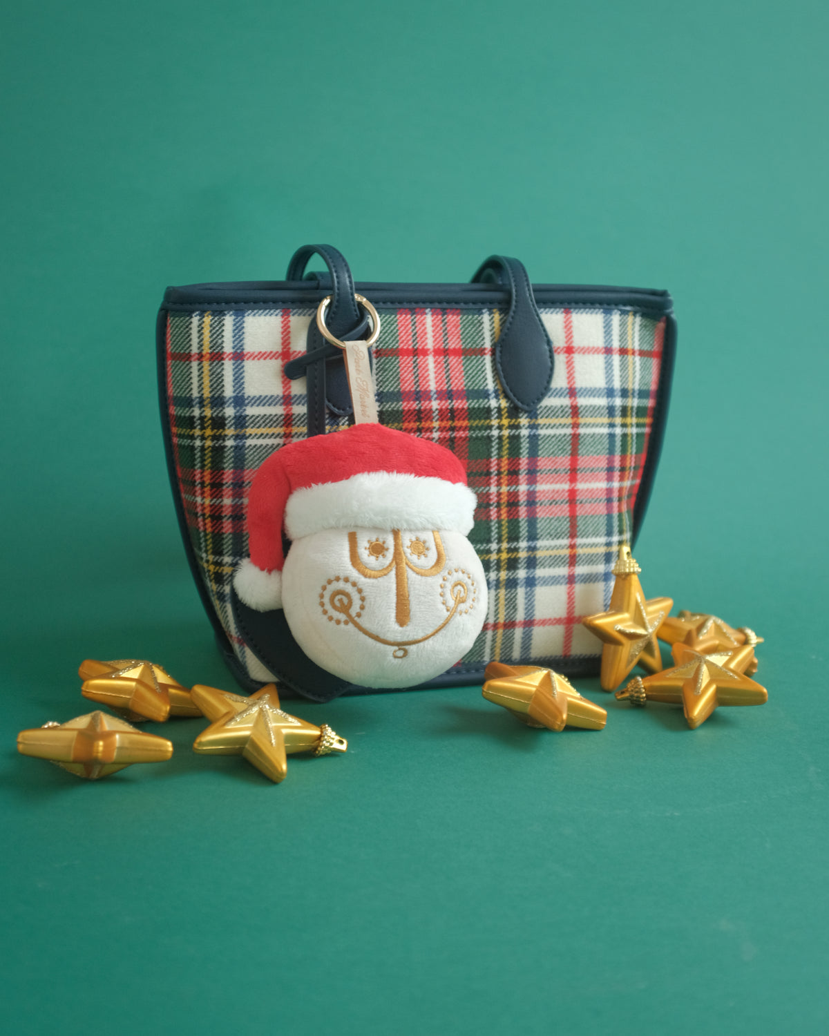 Tinsel Time bag charm on a plaid tote with gold star ornaments on a green backdrop