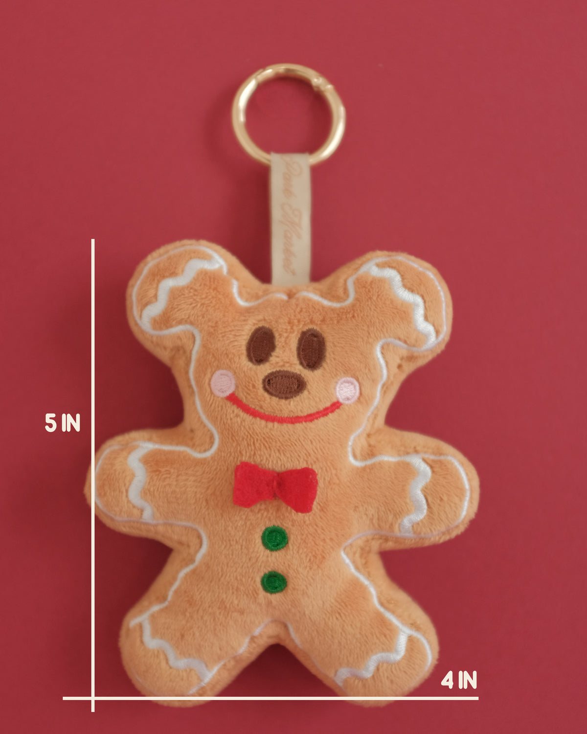 Gingerbread cookie plush bag charm with embroidered frosting and a red bow; measurement lines show 5 inches tall by 4 inches wide