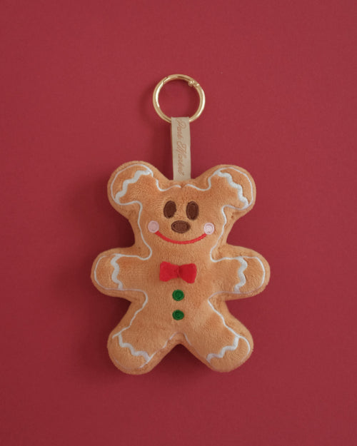 Gingerbread Gent plush bag charm with embroidered frosting, rosy cheeks and a red fabric bow tie, on a red background