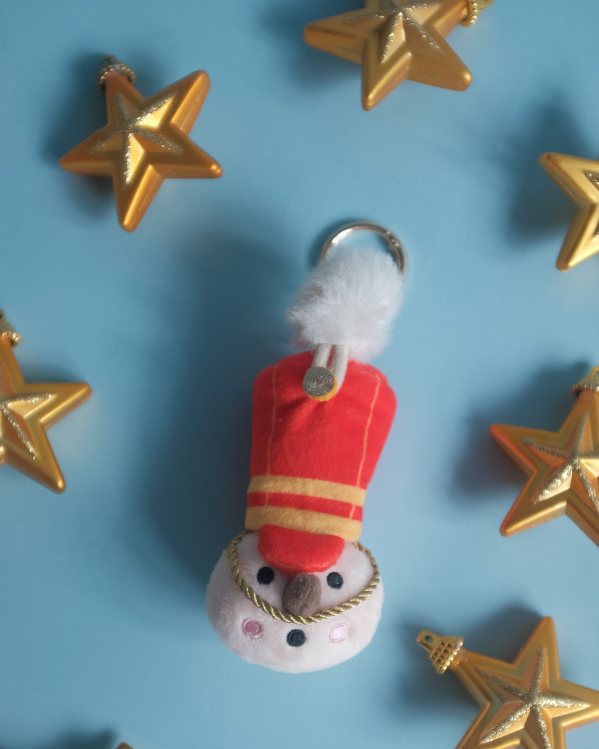 The Merry Marcher toy soldier bag charm surrounded by gold star ornaments on a blue backdrop
