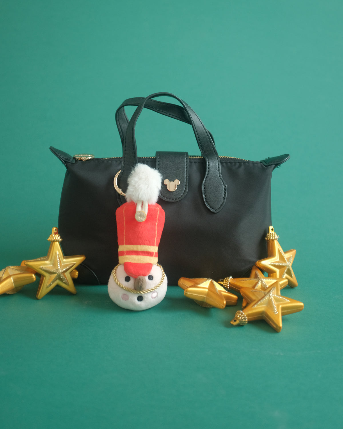 The Merry Marcher bag charm clipped to a black handbag, with gold stars on a green backdrop
