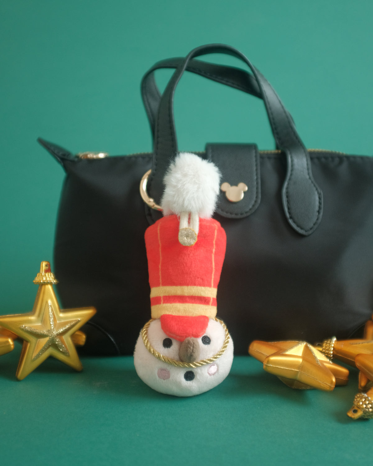 The Merry Marcher bag charm on a black handbag with gold star ornaments