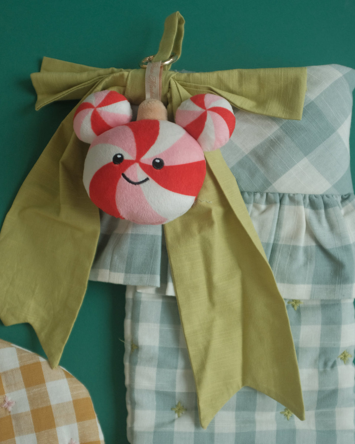 Peppermint Pal bag charm hanging from a green bow on a gingham Christmas stocking