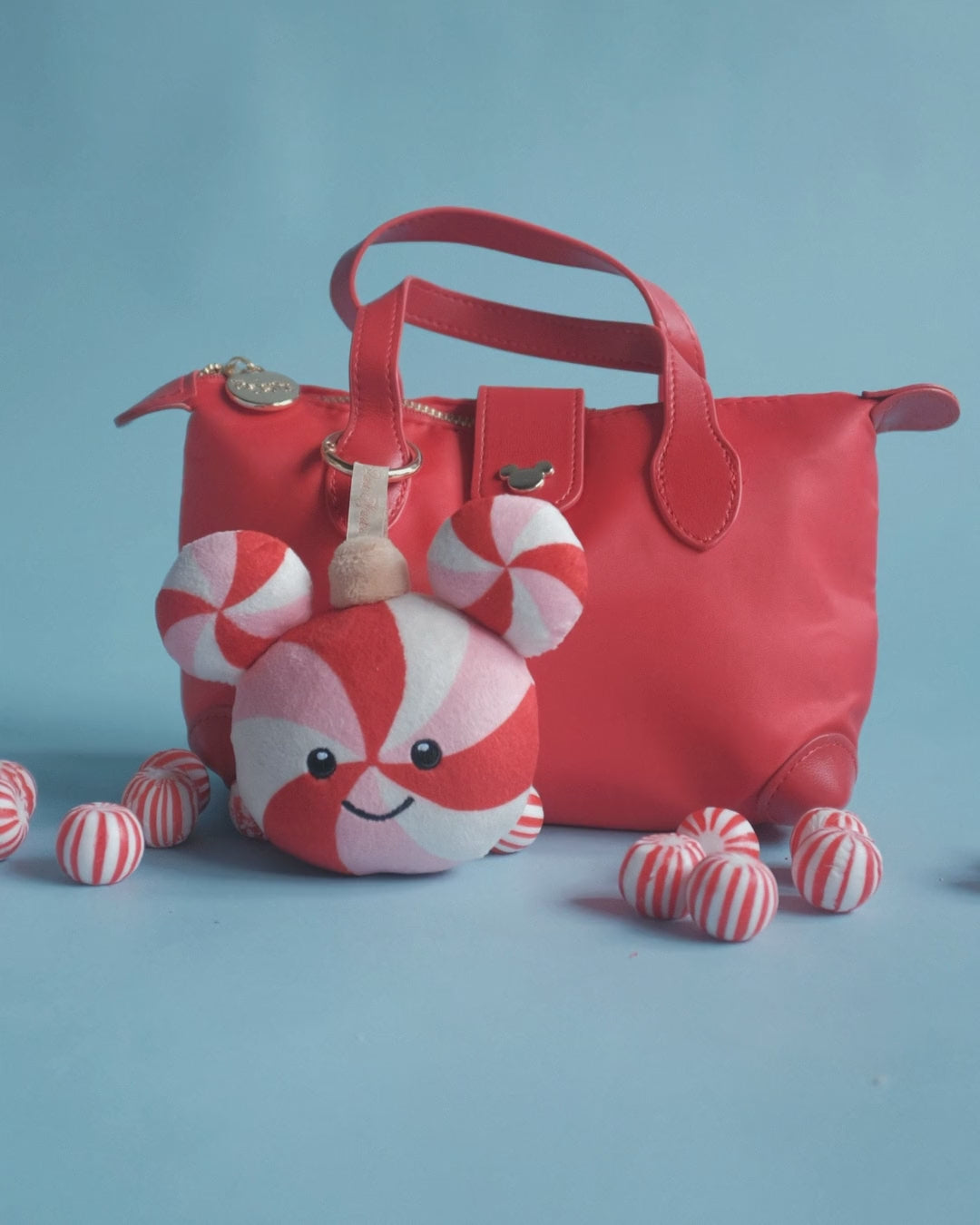 Peppermint Pal bag charm on set: clipped to a red bag, a candy flat-lay and peppermints tumbling in