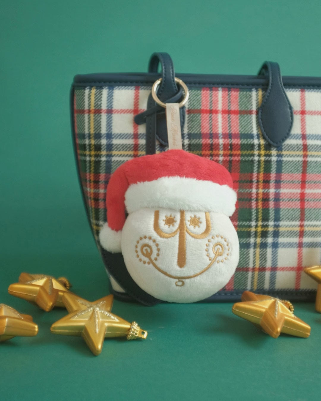 Tinsel Time bag charm on set: clipped to a plaid tote, a gold thread close-up, a pink bow and falling snow